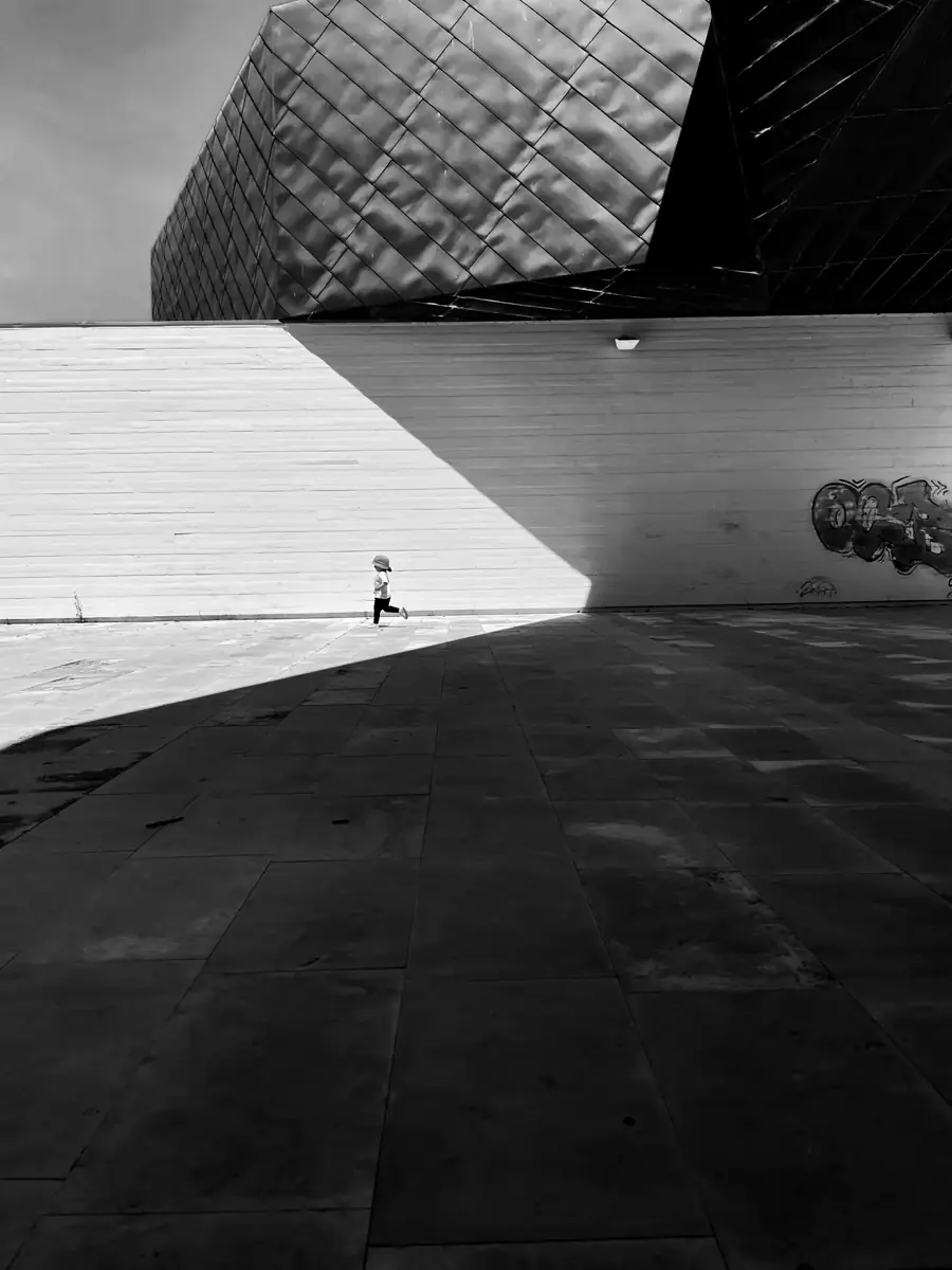 A small figure running across a wide, sunlit open plaza.