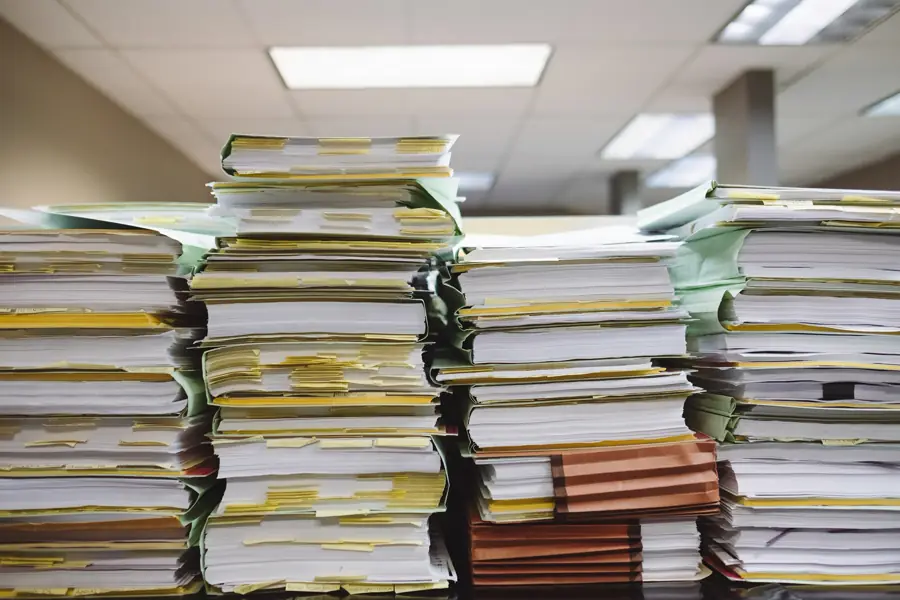 Tall stacks of paper files and folders piled on an office desk.