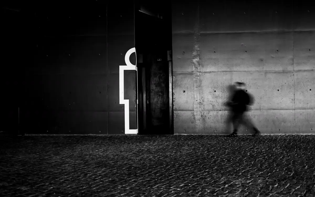 A blurred figure walking past an outlined human silhouette on a concrete wall.