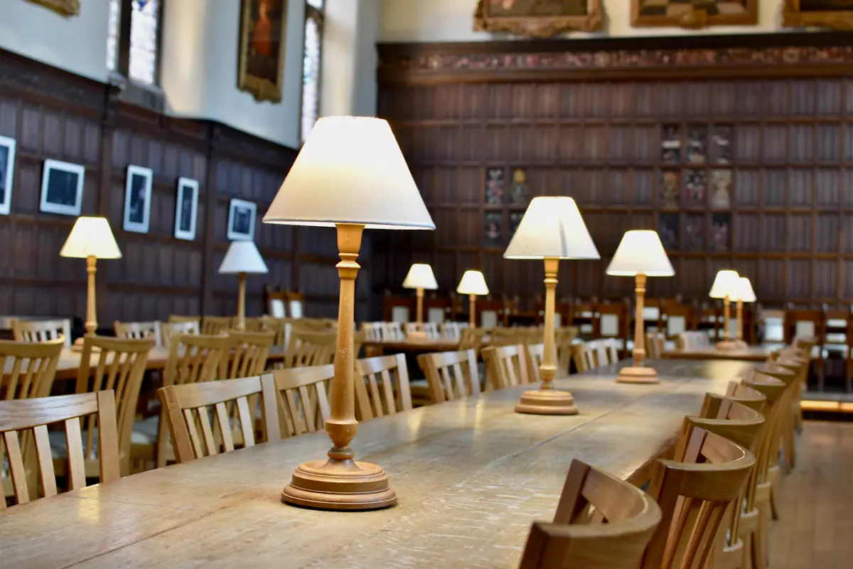 A long wooden table in a panelled reading room, a row of lamps along it.