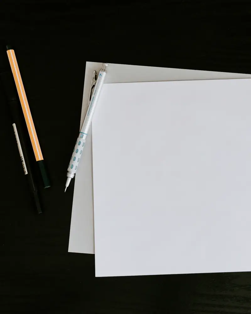 Blank sheets of paper and pens on a dark wooden table.