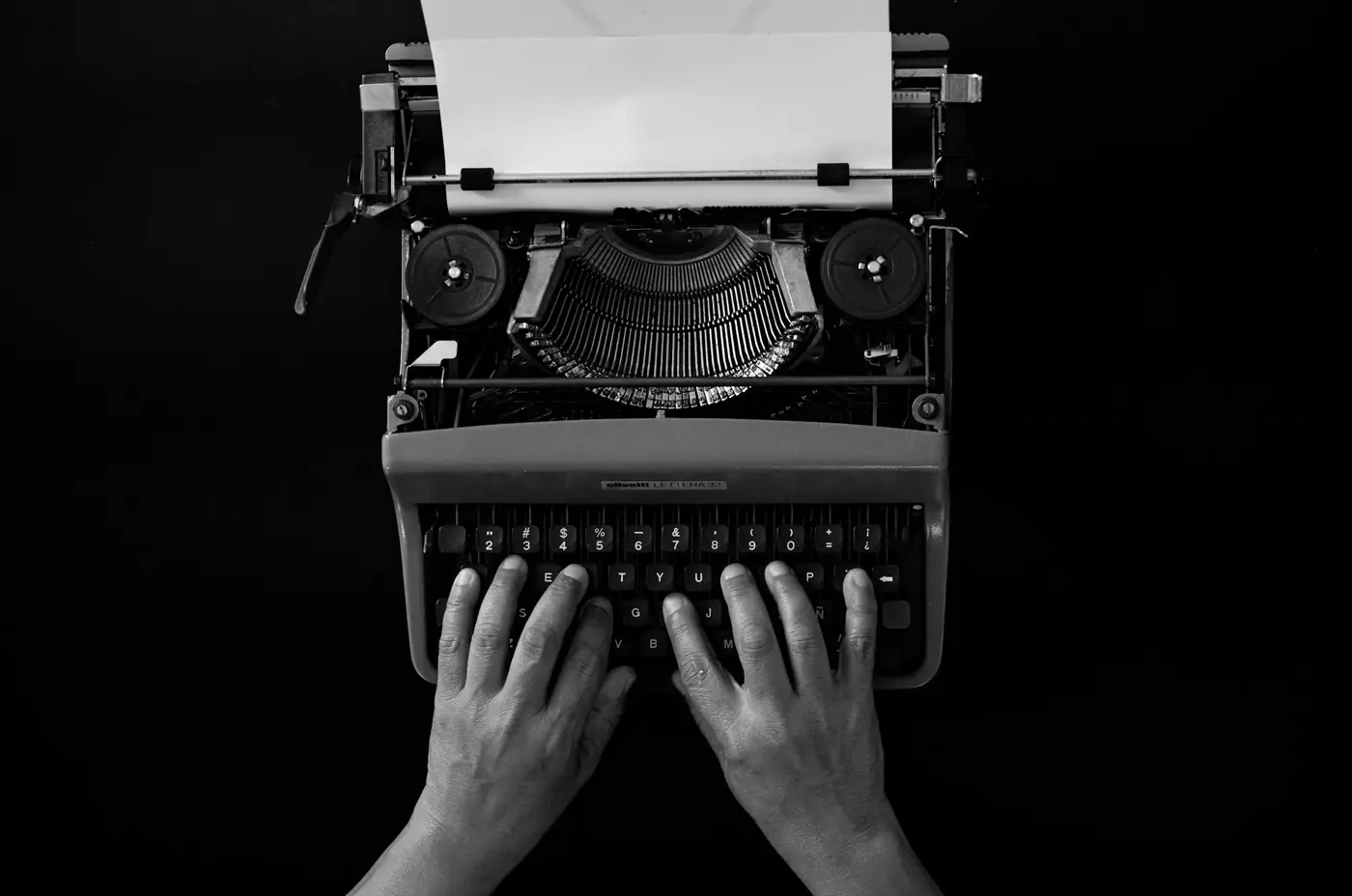 Hands typing on a typewriter with a blank sheet of paper, seen from above.